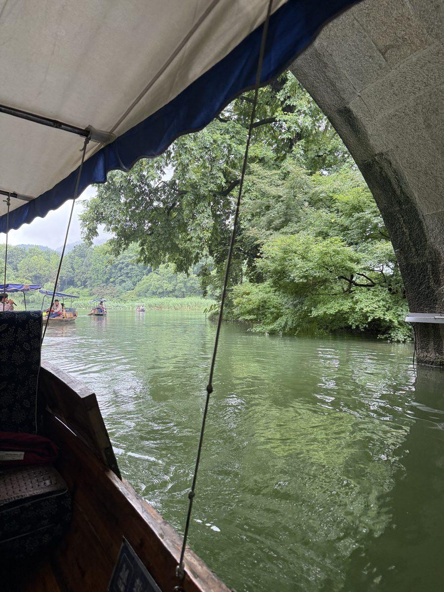 View from under the canopy of a hand-rowed boat passing a stone bridge on West Lake