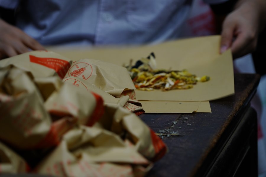 Individual herbal medicine packets wrapped in paper on a wooden counter