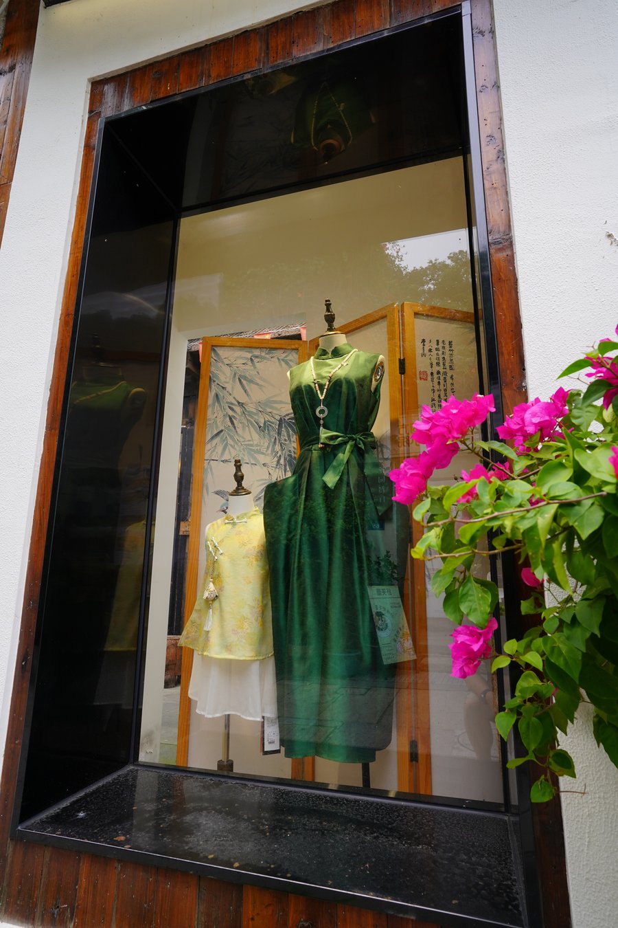 A shopfront window displaying handmade garments among climbing vines