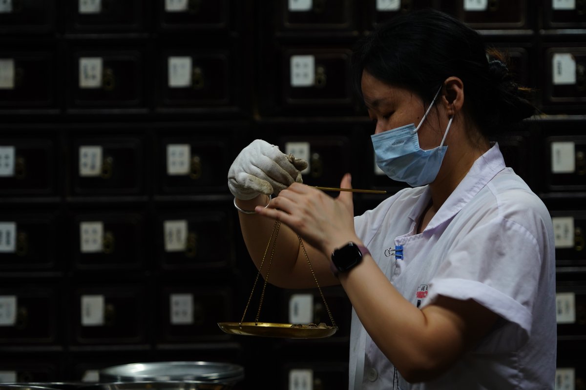 A pharmacist in a Qinghefang apothecary weighing herbs on a hand scale