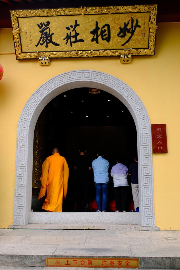 A plaque above an arched temple doorway with a monk passing through