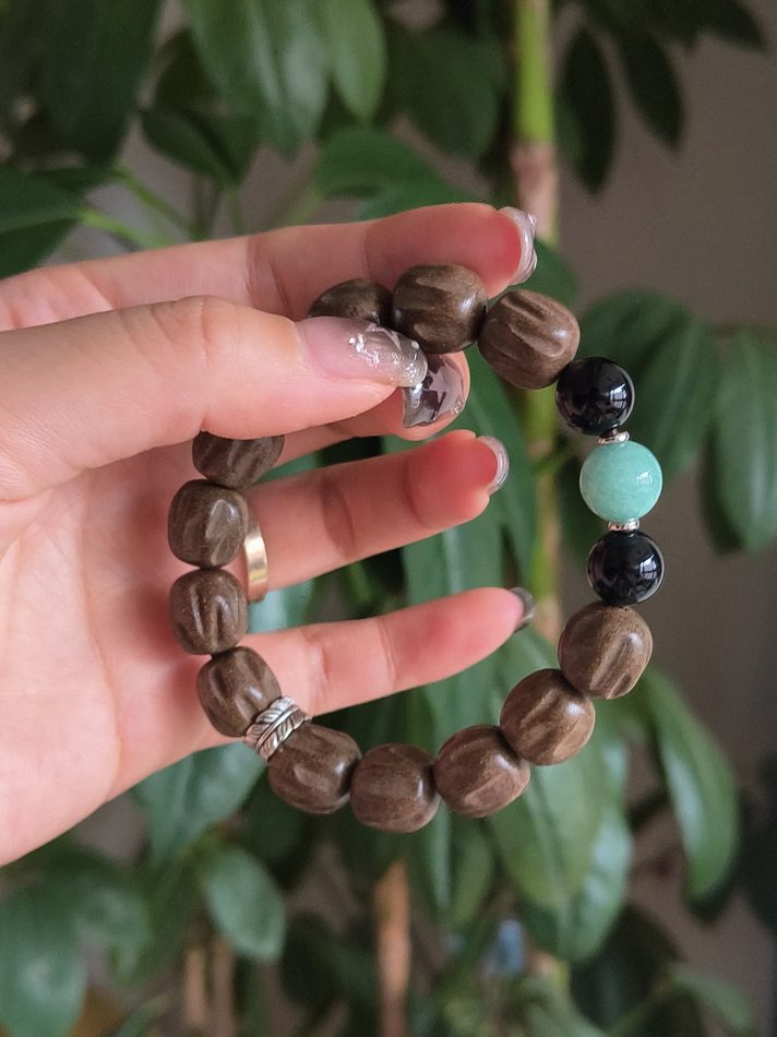 A hand holding a finished beaded bracelet against green leaves