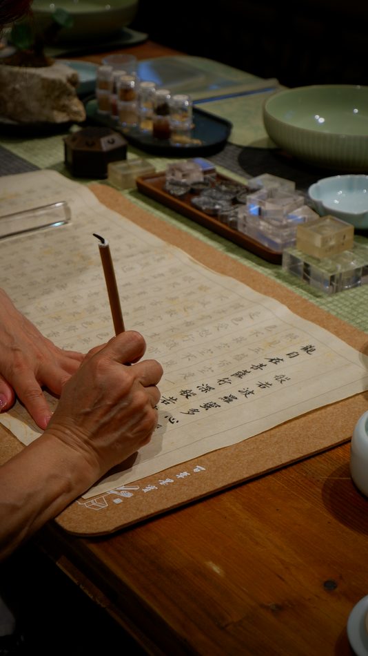 A hand writing with a brush beside a burning incense stick