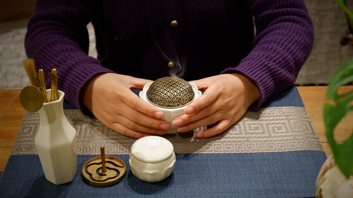 Hands cupping a lidded censer as incense smoke rises