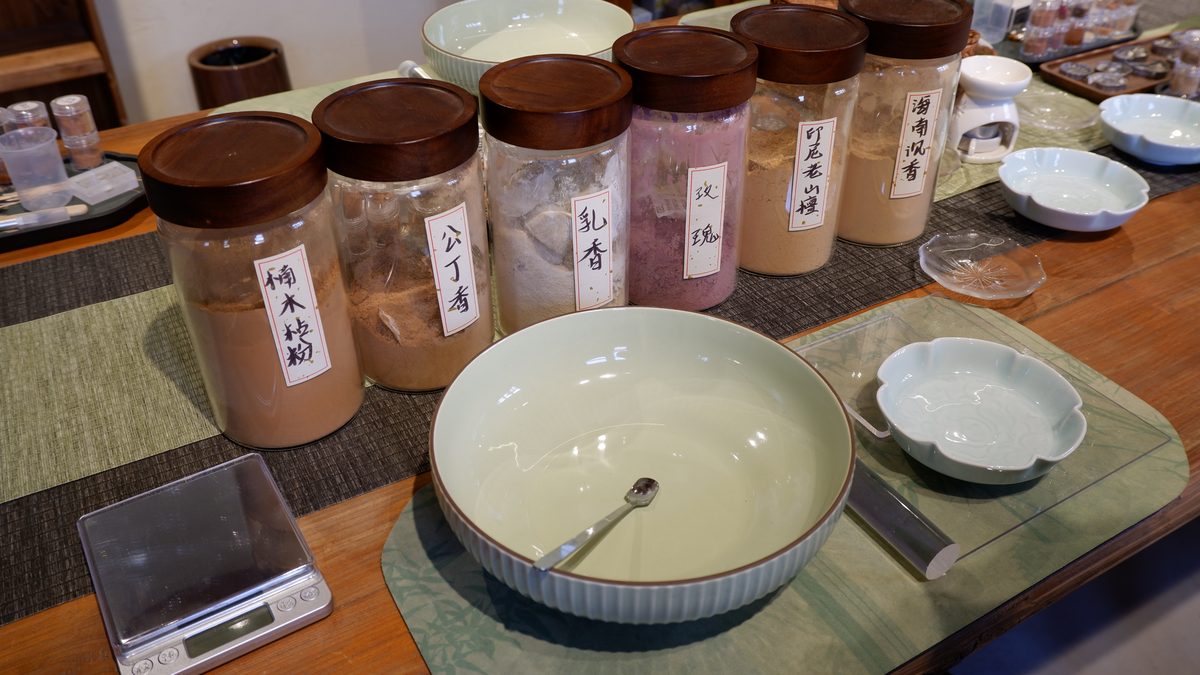 Labelled material jars beside a celadon bowl and a small scale