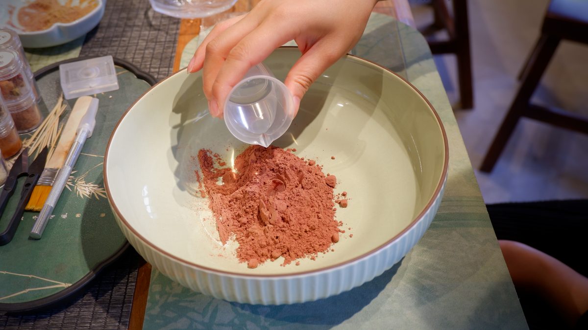 Water being poured into red incense powder in a celadon bowl