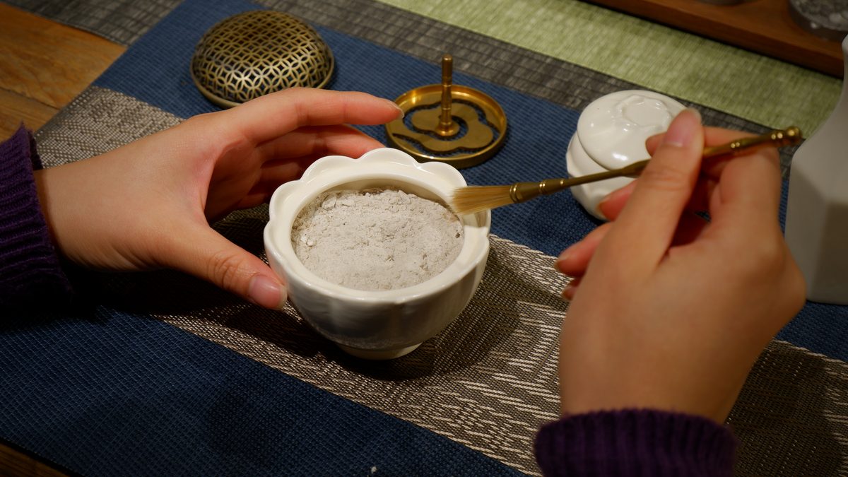 Hands levelling powdered incense in a small ceramic bowl