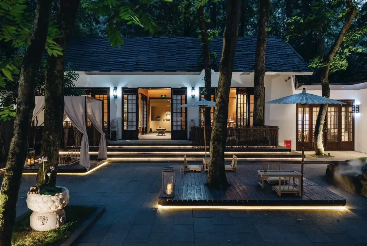 A lit courtyard house among trees in the evening
