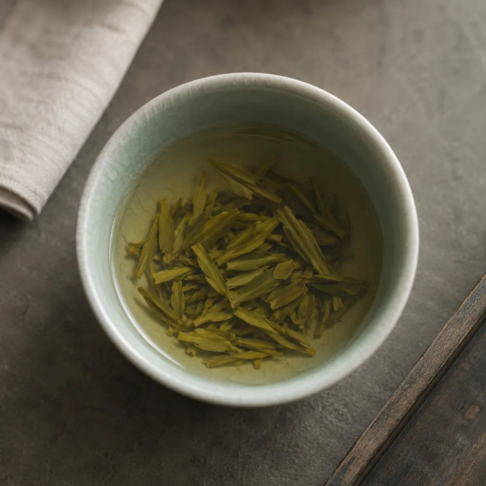 Longjing leaves steeping in a pale celadon cup on a stone surface