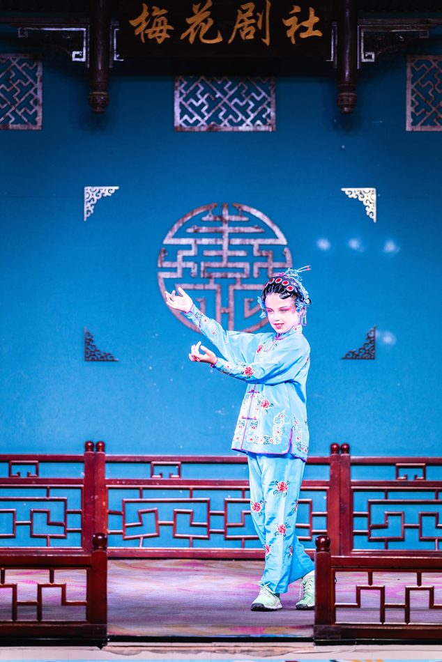A Sichuan-opera performer mid-movement on a blue stage