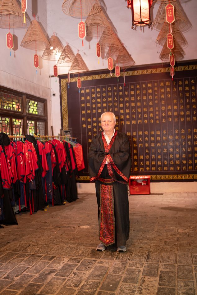 A figure in a long robe in a courtyard hung with red costumes