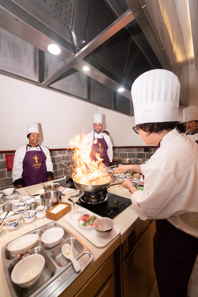 A cook tossing a wok over an open flame in the teaching kitchen
