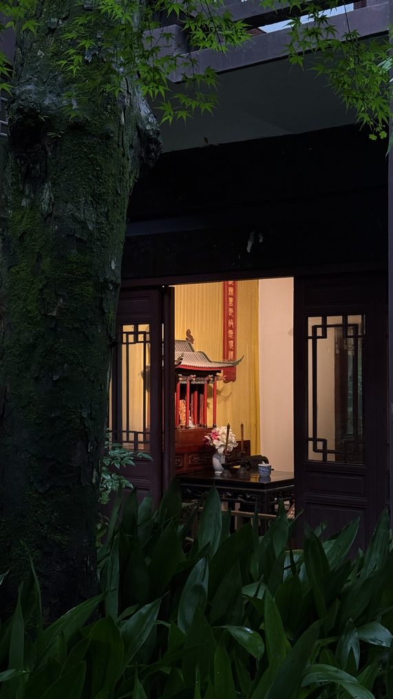 A lit temple side hall seen from a planted path at dusk
