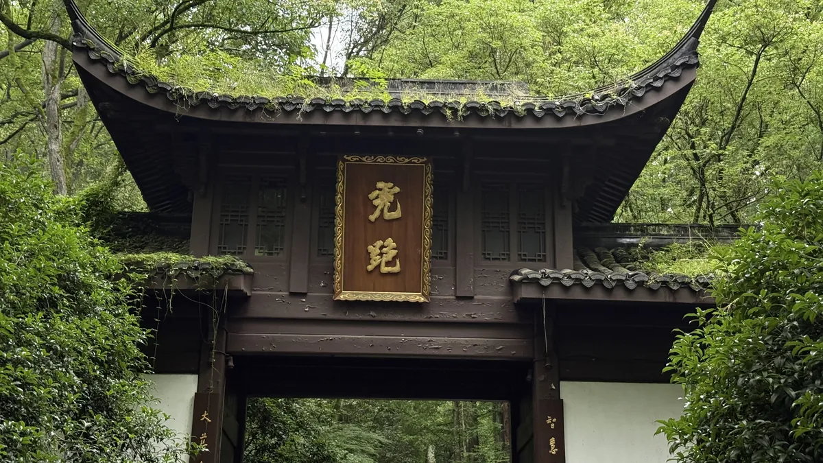 A timber temple gateway with a gold plaque, surrounded by dense green