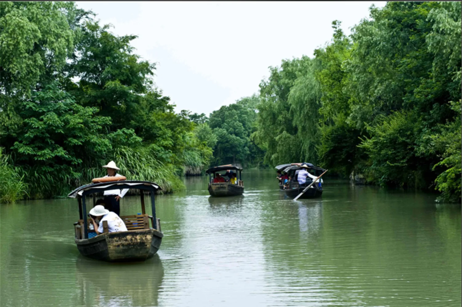 Small passenger boats travelling along a tree-lined waterway in Hangzhou