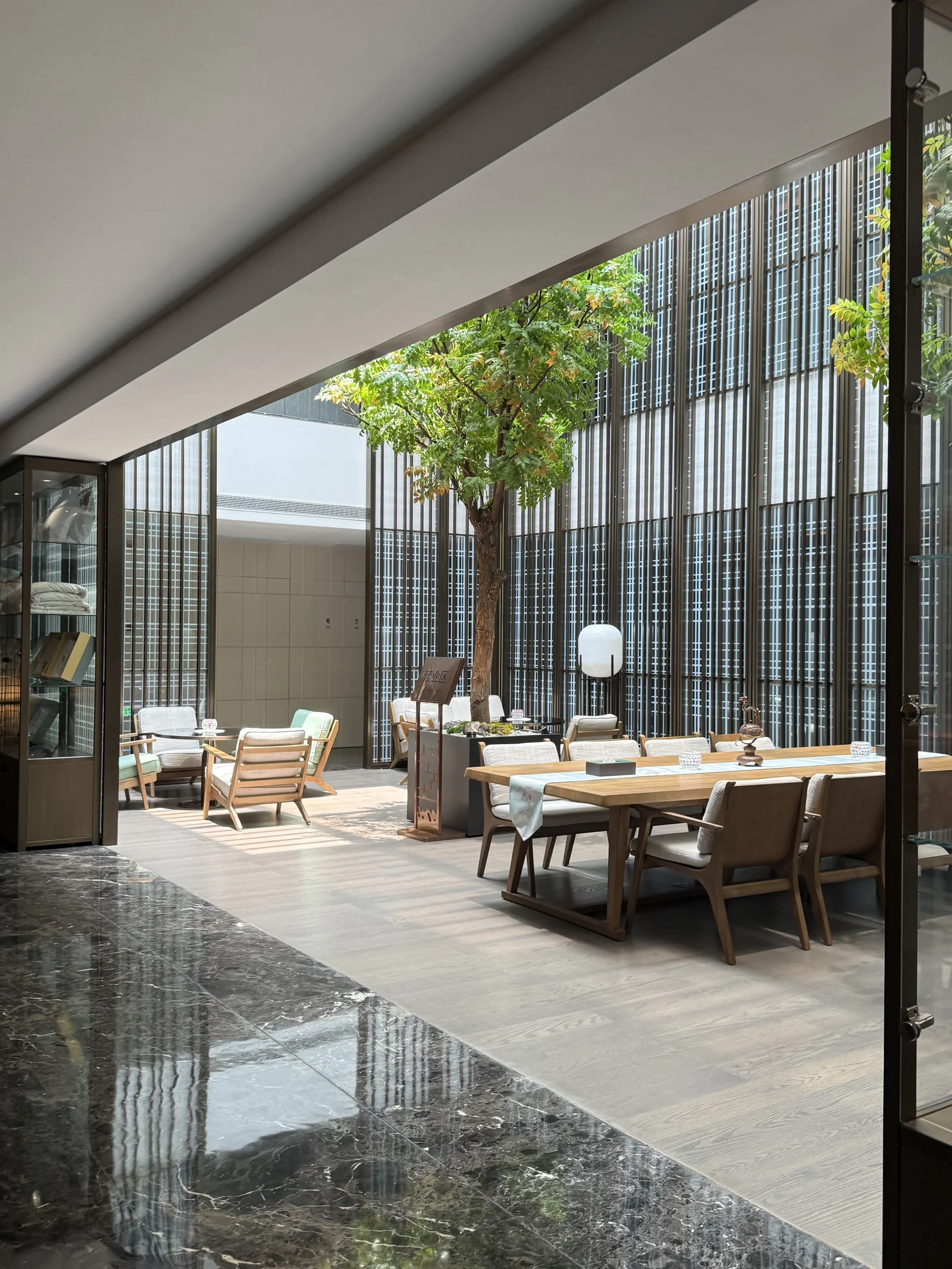 A sunlit courtyard seating area at Xizi Hotel, framed by trees and tall screens