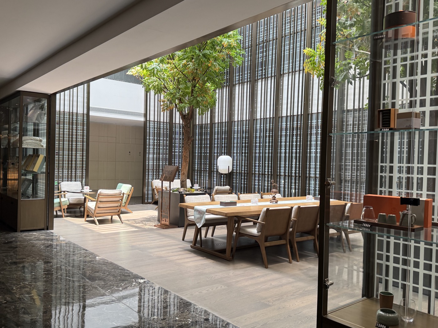 An open-air courtyard lounge with a mature tree and wooden dining furniture