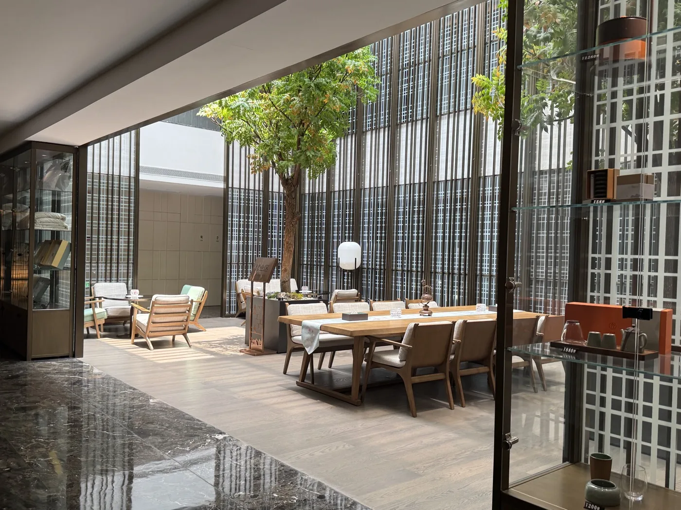 An open-air courtyard lounge with a mature tree and wooden dining furniture