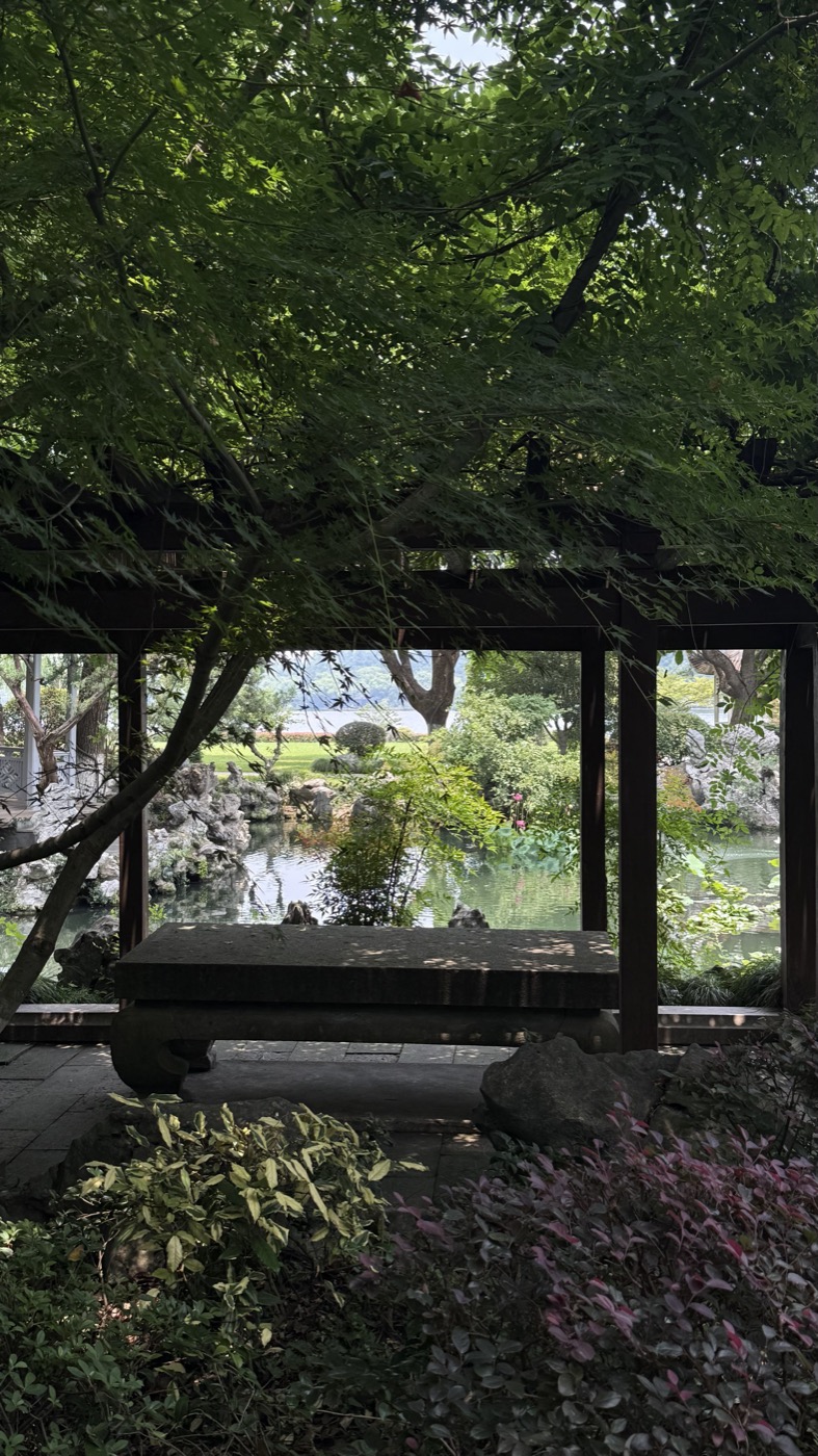 A stone table beneath a timber garden pavilion overlooking a pond