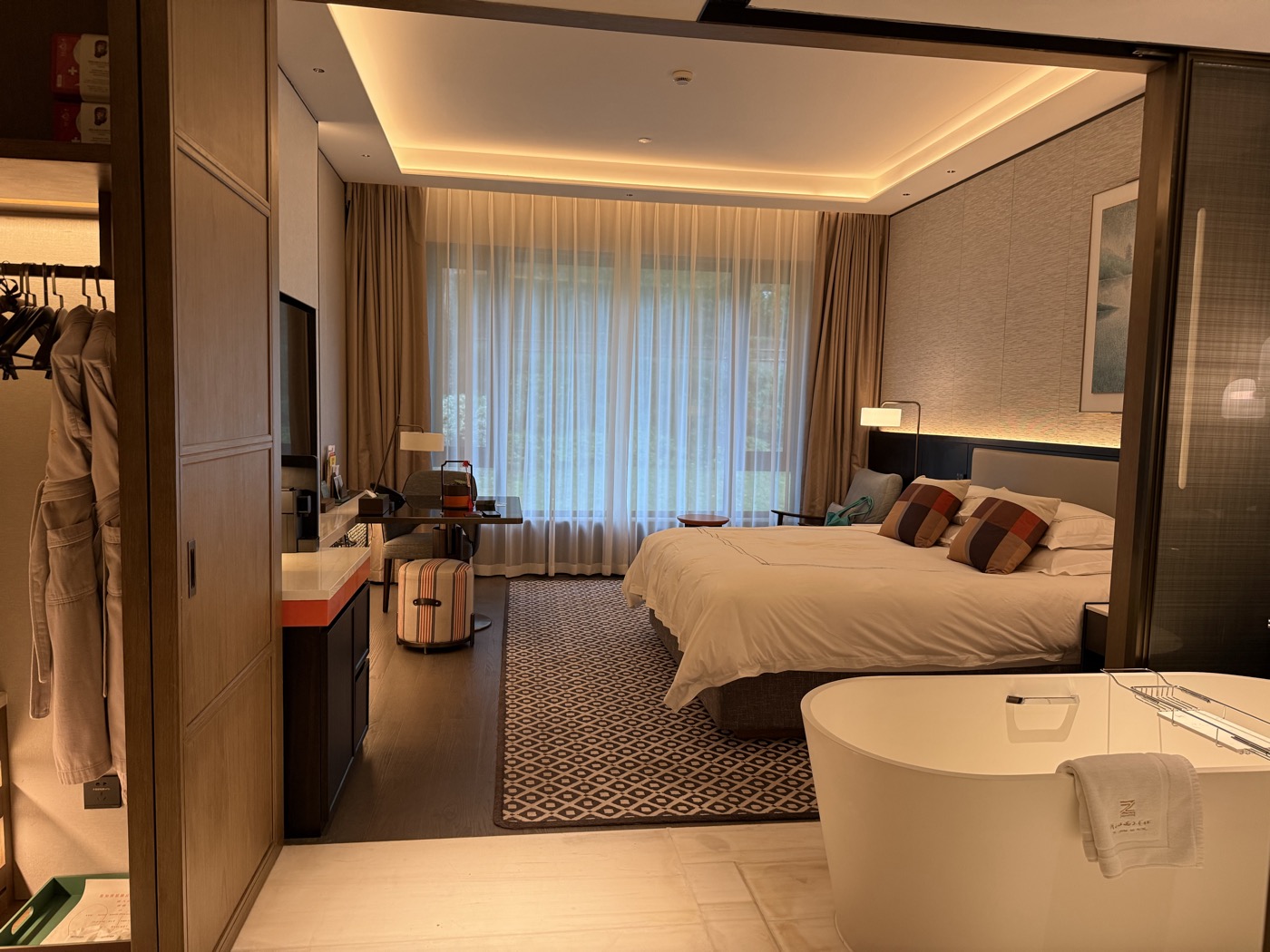 A hotel suite with a large bed and a freestanding bath beside floor-to-ceiling windows