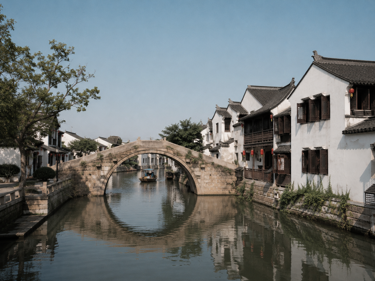 A stone bridge arching over a still canal in an old Chinese water town, white-walled houses mirrored in the water
